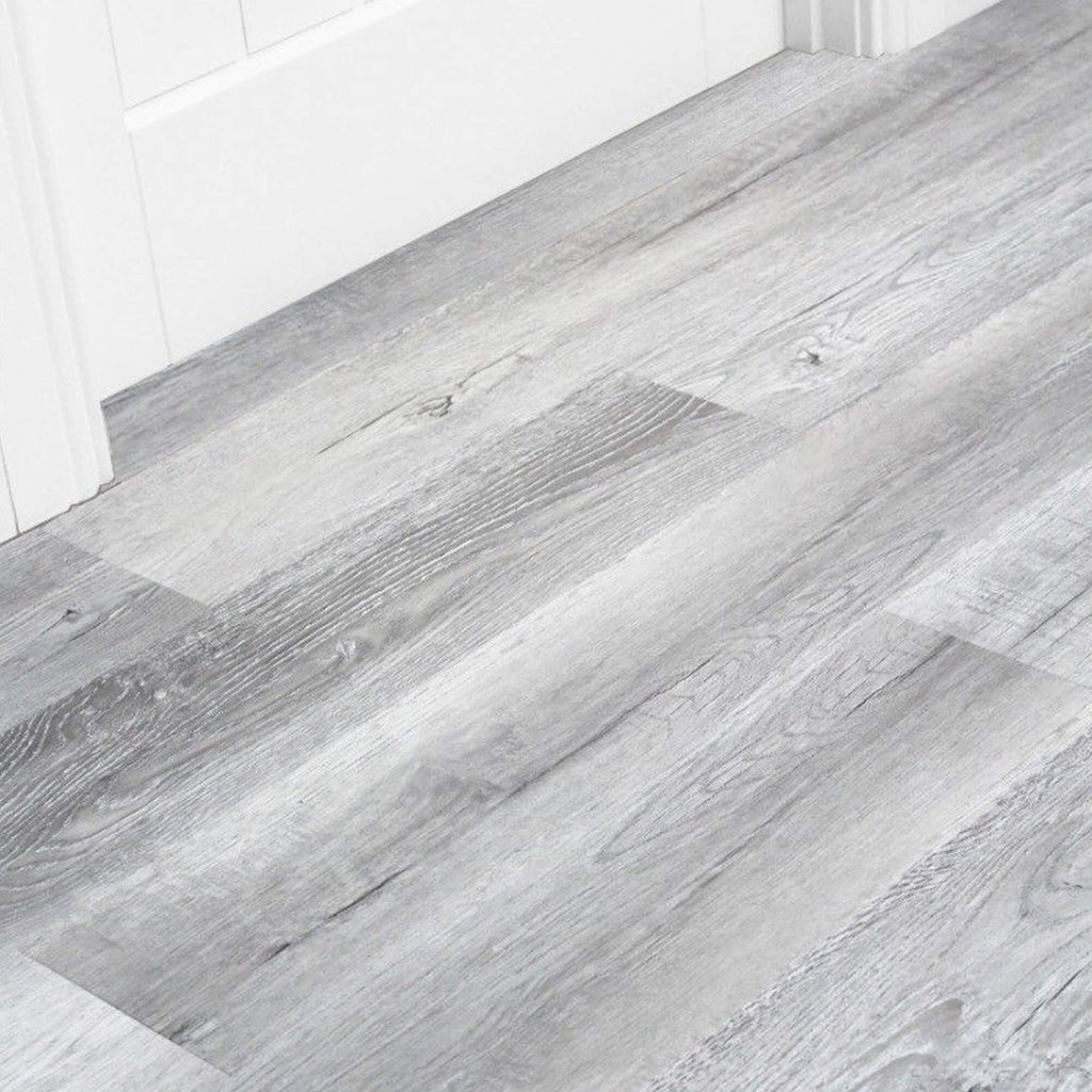Close-up of Bamburgh Grey Rigid LVT  flooring in a room with white skirting boards and a white door.