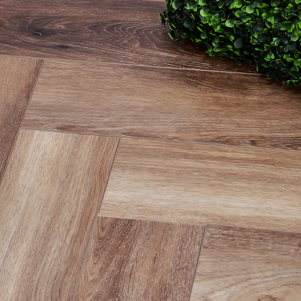Close-up of Fumed Oak Rigid LVT Herringbone Flooring with a green plant in the corner.