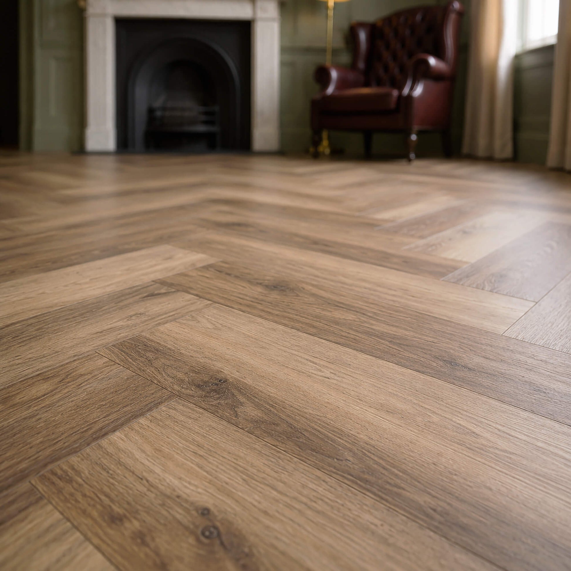 Close-up of a victorian living room with Fumed Oak Rigid LVT herringbone flooring with a fireplace and leather chair.