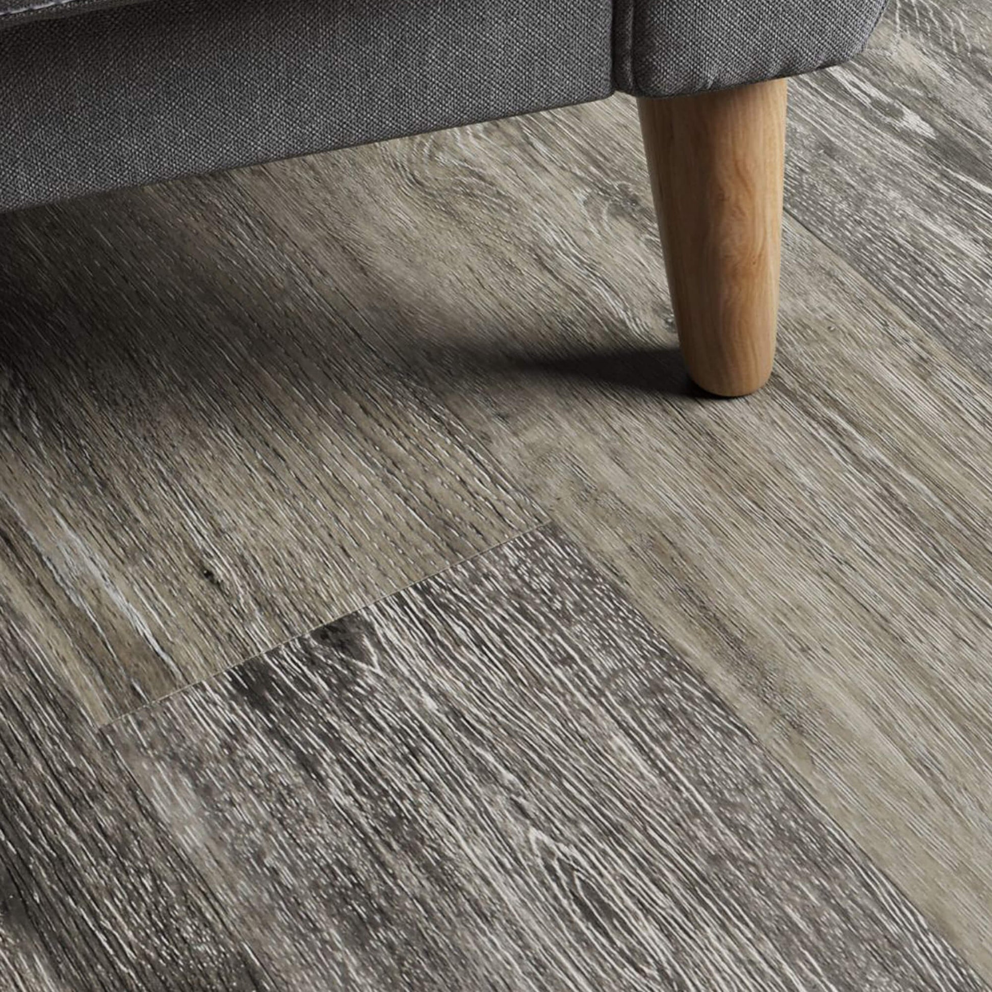 Close-up of a Portland Oak Rigid LVT flooring with a grey sofa leg in the foreground.
