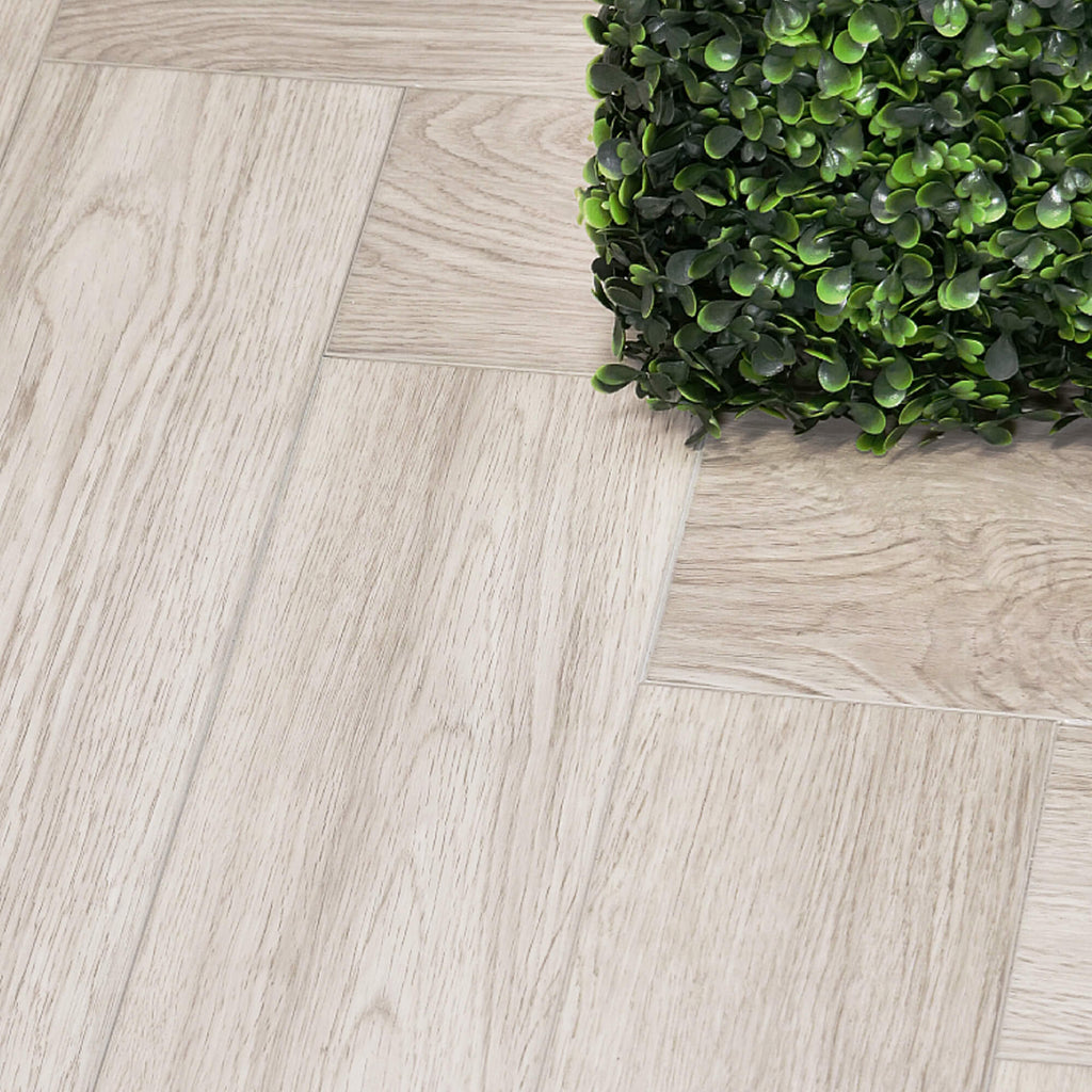 Close-up of Siberian Oak Rigid LVT Herringbone Flooring with a green plant in the corner.